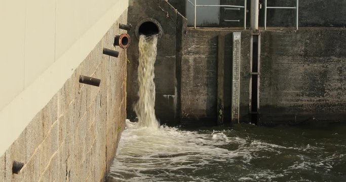 Water spilling out pumped through a pipe at water reservoir dam and hydroelectric power station