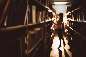 Blur background of young lady with long hair in casual clothing trying to get book from the highest shelf at dark bookstore. Beautiful woman choosing literature for gaining new knowledge.