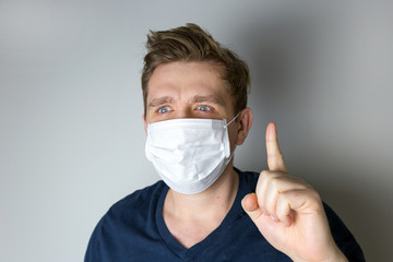 Man with mask to protect him from virus. The concept of the epidemic of the coronavirus. Tired crazy Doctor with medical white mask showing point sign with his hand