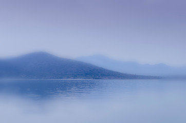 Fototapeta premium An abstract blurry blue seascape with two mountain rages and water foreground suitable as background with plenty of copy space. 