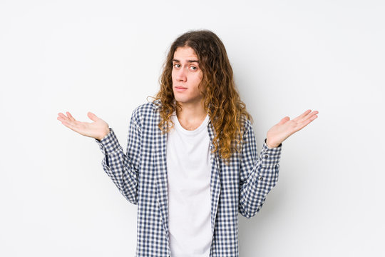 Young long hair man posing isolated doubting and shrugging shoulders in questioning gesture.