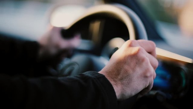 Color close-up footage of a man's hand on a car steering wheel.