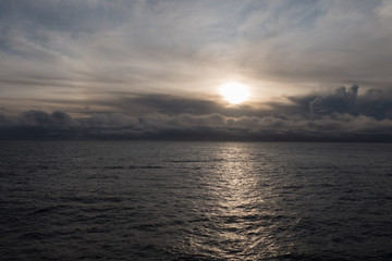 Fototapeta na wymiar Sonnenuntergang mit dramatischem Wolkenhimmel im Fjord von der Seeseite aus