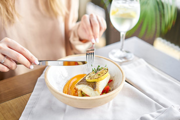 Roasted Halibut with vegetables, paprika pepper and pumpkin cream. Lunch in a restaurant, a woman eats delicious and healthy food. Dish decorated with a slice of lemon. Restaurant menu