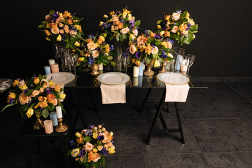 a large flower arrangement with candles on a transparent glass table with white gilded plates and gilded forks, knives and glasses. floral table decoration with expensive dishes