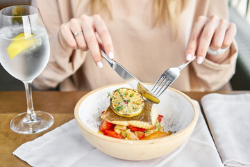Roasted Halibut with vegetables, paprika pepper and pumpkin cream. Lunch in a restaurant, a woman eats delicious and healthy food. Dish decorated with a slice of lemon. Restaurant menu