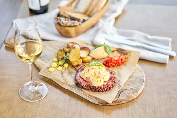 Roasted octopus BBQ and Baked potato with a glass of Grapa. Wooden plate. Restaurant menu