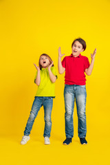 Fototapeta premium Astonished. Happy children playing and having fun together on yellow studio background. Caucasian kids in bright clothes looks playful, laughting, smiling. Concept of education, childhood, emotions.