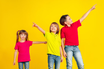 Pointing. Happy children playing and having fun together on yellow studio background. Caucasian kids in bright clothes looks playful, laughting, smiling. Concept of education, childhood, emotions.