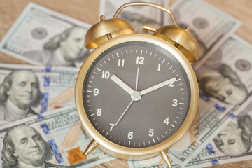 Old fashioned twin bell alarm clock with hundred dollar bills in background. Time is money.