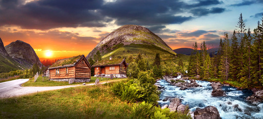 Beautiful magic forest with two wooden houses near blue wild river in the sunset view. Amazing evening norway country panomama. - obrazy, fototapety, plakaty