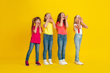 Obraz premium Calling. Happy children playing and having fun together on yellow studio background. Caucasian kids in bright clothes looks playful, laughting, smiling. Concept of education, childhood, emotions.