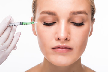 Beautiful young woman gets beauty injection in eye area from sergeant isolated over white background.