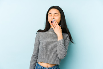 Young chinese woman isolated on a blue background yawning showing a tired gesture covering mouth with hand.