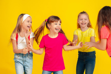 Happiness. Happy children playing and having fun together on yellow studio background. Caucasian kids in bright clothes looks playful, laughting, smiling. Concept of education, childhood, emotions.