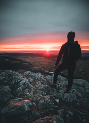 Hiker with backpack relaxing on top of a mountain and enjoying sunrise