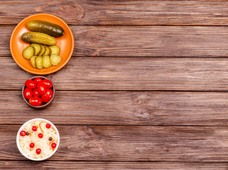 Homemade tasty fermented milk products on plates - sauerkraut, tomatoes, pickles, on wooden background, copy space. Flat lay.