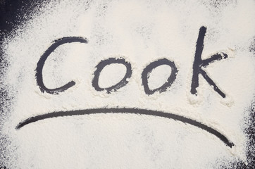words Cook written on a black background with flour. Inscription.