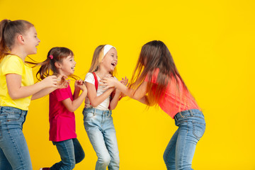 Happiness. Happy children playing and having fun together on yellow studio background. Caucasian kids in bright clothes looks playful, laughting, smiling. Concept of education, childhood, emotions.