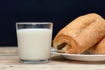Glass of milk, two buns on a white plate close-up on a wooden background with copy space on a black...