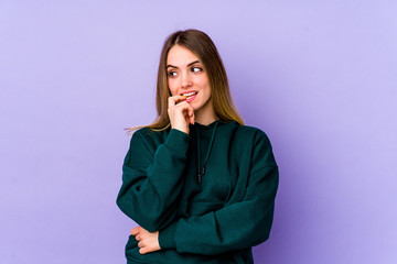 Fototapeta na wymiar Young caucasian woman isolated on purple background relaxed thinking about something looking at a copy space.