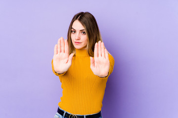 Young caucasian woman isolated on purple background standing with outstretched hand showing stop sign, preventing you.