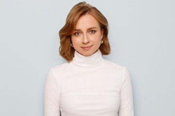 Obraz premium Close up portrait of joyful woman with short hair wears turtleneck, poses and looking at camera, blue background. European female, facial expressions