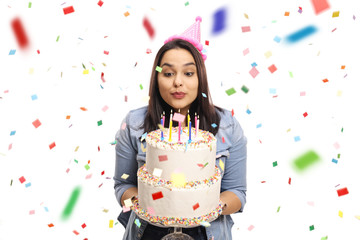 Young female celebrating birthday and blowing candles on a cake with confetti around