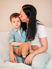 Mother and her little 5 years old kid sitting on sofa, mother kisses her child on the forehead. Mother's day concept