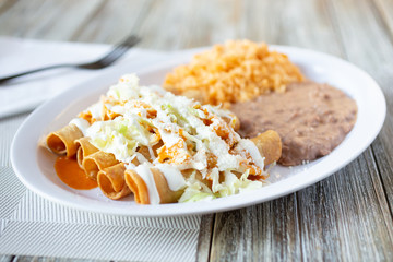 A view of a taquitos plate in a restaurant or kitchen setting, featuring a side of rice and beans.
