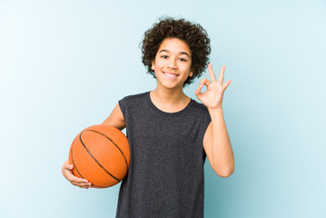 Kid boy playing basketball isolated on blue background cheerful and confident showing ok gesture.