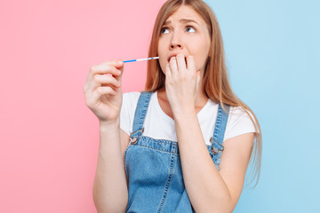Shocked terrified young woman holds a pregnancy test - obrazy, fototapety, plakaty