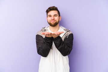 Young man isolated on purple background holding something with palms, offering to camera.