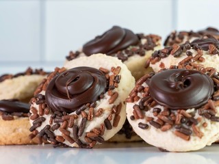 Chocolate thumbprint cookies with sprinkles and frosting piled up against a white subway tile...