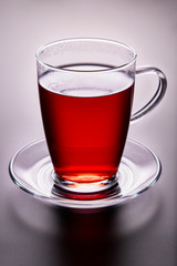 Close-up of tea glass with red fruit tea, on a glass saucer. Backlight illuminated.