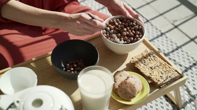 Breakfast on the terrace. Picnic on the sunny terrace. Healthy breakfast. Girl puts chocolate corn balls in a bowl. Tasty healthy breakfast with flakes, milk and cookies. Morning tea. Eco products. 