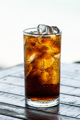 fresh cola drink with ice in glass on wood table