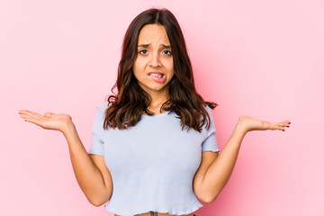 Young mixed race hispanic woman isolated confused and doubtful shrugging shoulders to hold a copy...