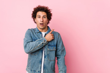 Curly mature man wearing a denim jacket against pink background pointing to the side