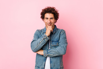 Fototapeta na wymiar Curly mature man wearing a denim jacket against pink background smiling happy and confident, touching chin with hand.