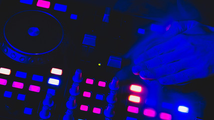 Fototapeta na wymiar DJ plays music. sound mixer controller with knobs and sliders. hands on the mixing deck with turntables at dark with illuminated controls