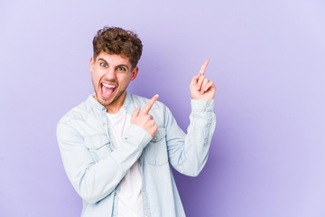 Young blond curly hair caucasian man isolated pointing with forefingers to a copy space, expressing excitement and desire.