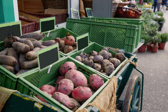 Outdoor view of various type of potatoes sell on shelf over green cart stall in front of grocery store beside outdoor sidewalk of open air market.