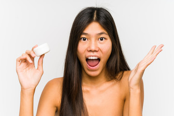 Young chinese woman holding a moisturizer isolated celebrating a victory or success