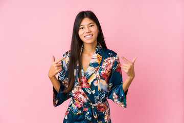 Young asian woman wearing a kimono pajamas smiles, pointing fingers at mouth.