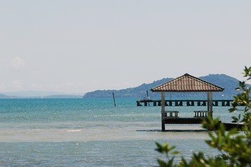 Perspective view of a wooden pier on the seashore with clear blue sea and blue sky