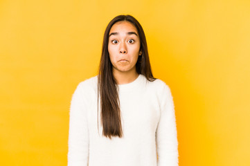 Young woman isolated on a yellow background shrugs shoulders and open eyes confused.