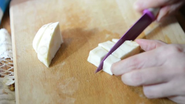Cutting celery root in pieces on a cutting board.