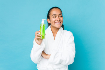 Young mixed race indian holding an aloe vera bottle smiling confident with crossed arms.