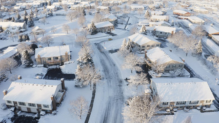Aerial view of residential houses covered snow at winter season. Establishing shot of american neighborhood, suburb.  Real estate, drone shots, sunny morning, sunlight, from above.